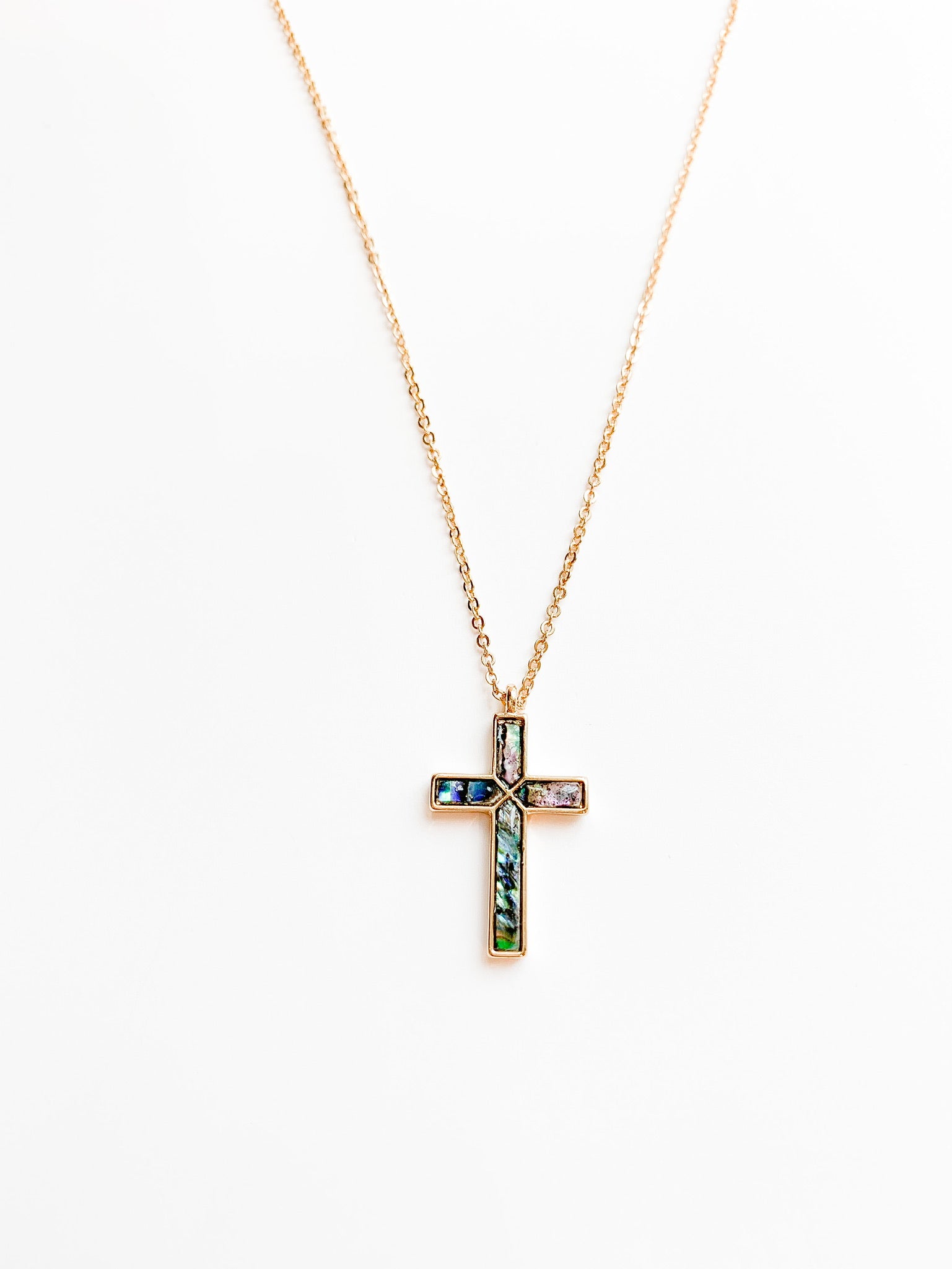 Delicate gold necklace featuring a cross pendant with luminous abalone shell inlay, displaying natural ocean-inspired hues of blue, green, and pearl.