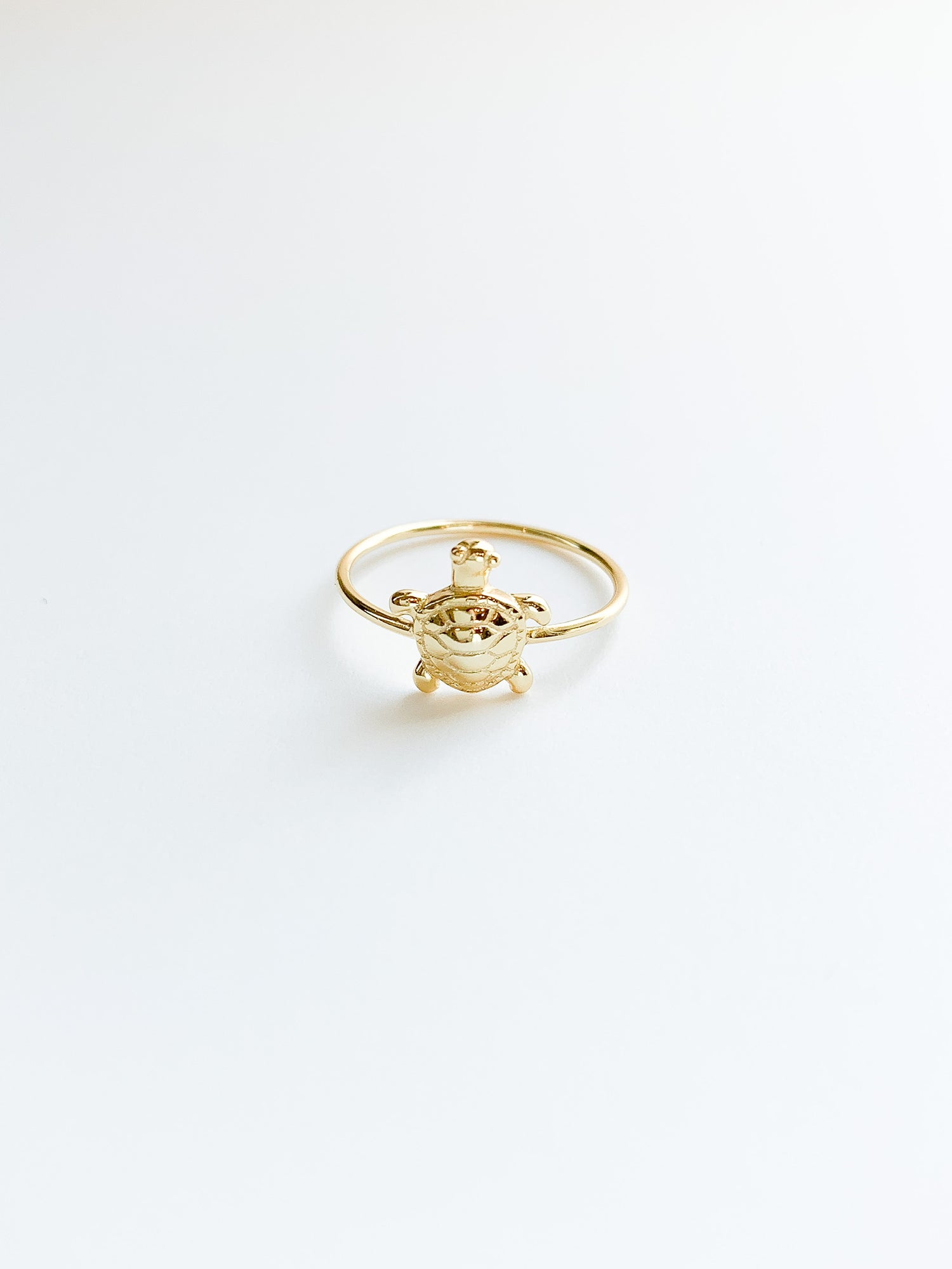 A gold-colored turtle-shaped ring against a white background.